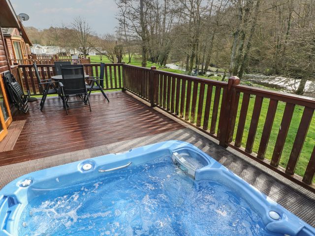 A hot tub on a deck with chairs and table at Riverside Lodge 3