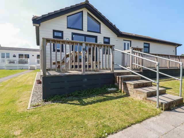 A single-story house with wooden railings and steps leading to the entrance at Lodge 18 in St Merryn