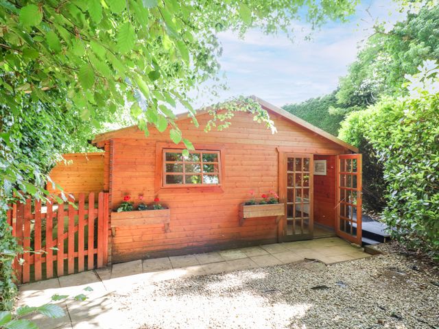 A wooden building with a door and window in an outdoor area at Stumps Cross Lodge Upper Coscombe near Winchcombe