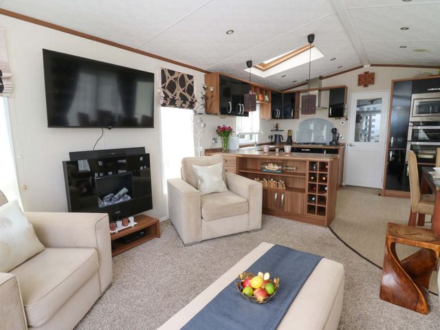 A living room featuring a television, sofa, and open kitchen at Ty Seren, New Quay
