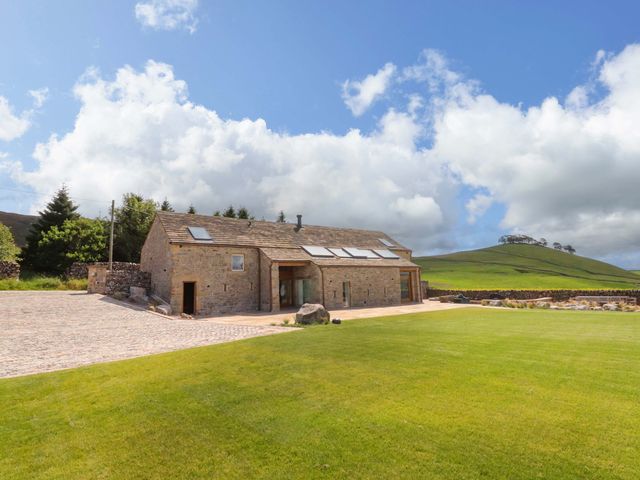 A stone house with a cobblestone driveway and lawn at Carden Laithe Barn Threshfield