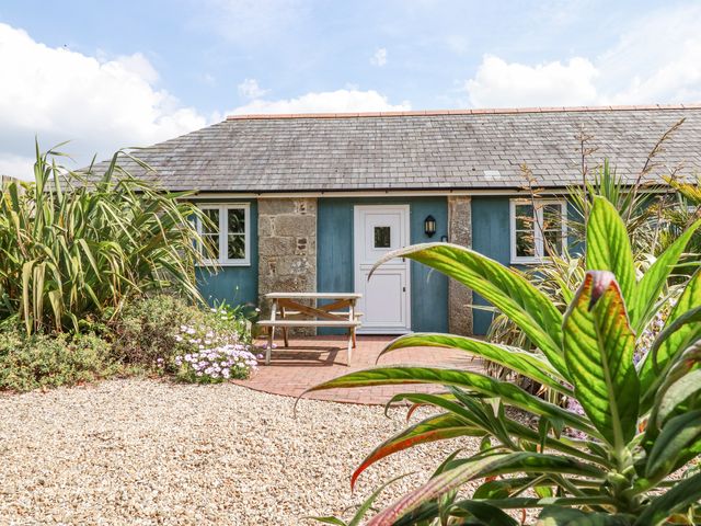The exterior of a stone and wood cottage with a white door and two windows a wooden picnic table and plants in front at Roses Stable Bodrean near Truro