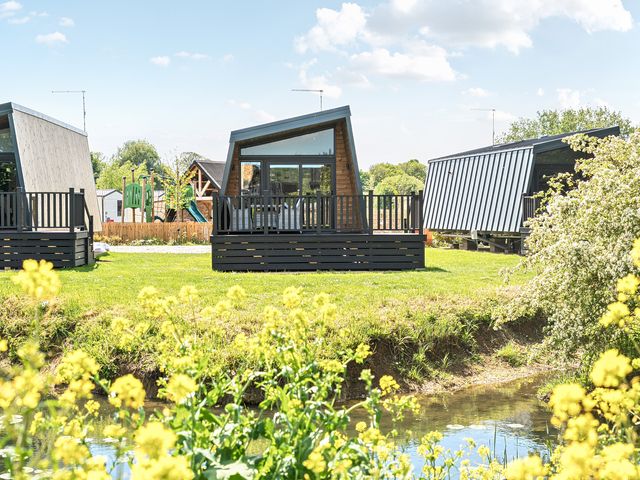 Three modern cabins with slanted roofs near a small water body and yellow flowers at Starlight Skylight - Billing Aquadrome Holiday Park