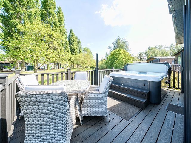 An outdoor deck with a table and four chairs and a hot tub at Lakeside Lullaby  Billing Aquadrome Holiday Park
