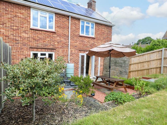 A backyard garden with a wooden picnic table and umbrella beside a brick house with solar panels at 3 Birkbeck Way in Norwich