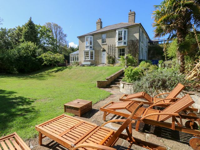 A garden with lounge chairs and a house in the background at Woodlands in Freshwater