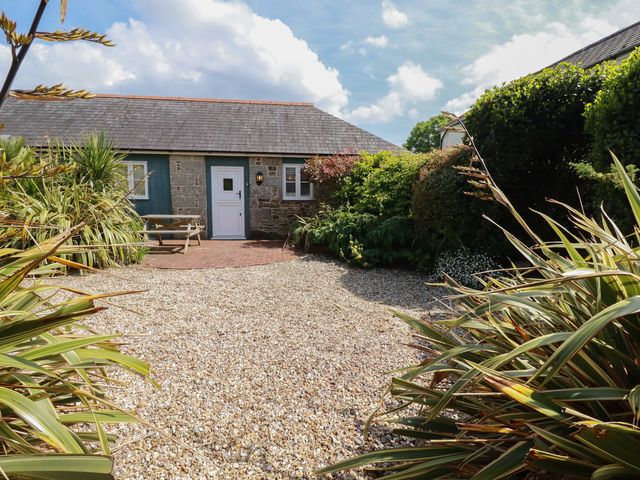 A gravel courtyard with plants and shrubs surrounding a stone building with a white door and window at The Copper House in Bodrean near Truro