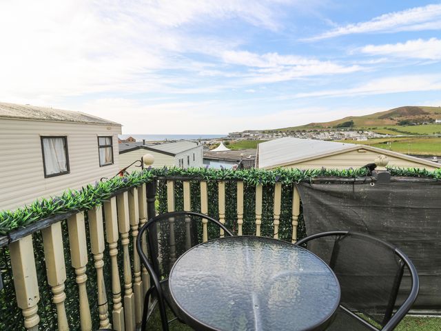 A balcony with a glass table and two black chairs overlooking caravans and hills at GM18 Clarach Bay near Aberystwyth