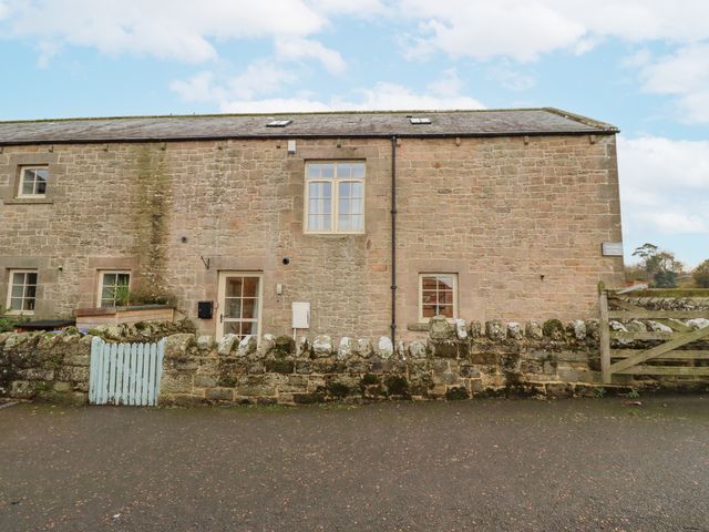 An exterior view of a stone building with windows and a gate at Watermill Cottage in North Charlton