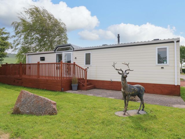 A mobile home with a deck and a statue of a deer at Plot 12 in Carlisle
