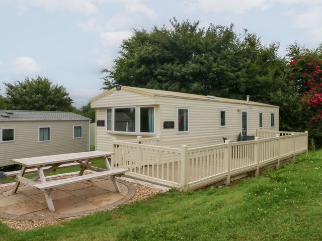 A mobile home with a deck and table at Mountain View in Pwllheli