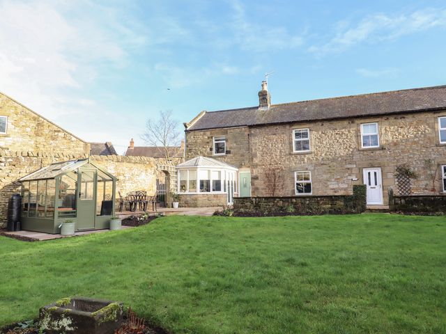A garden with a greenhouse and building at Linn Cottage in Hexham
