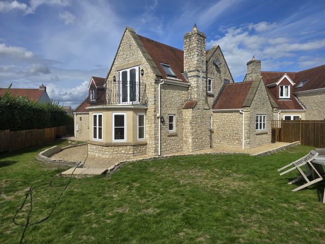 A stone house with a lawn and surrounding fence at The Mill House in Glastonbury