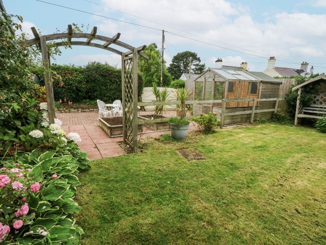 A garden with a greenhouse and seating area at 1 Maes Y Ffynnon in Llandegfan