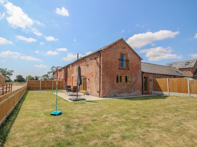 A brick building with a patio and grass area at Willow Barn in Shrewsbury