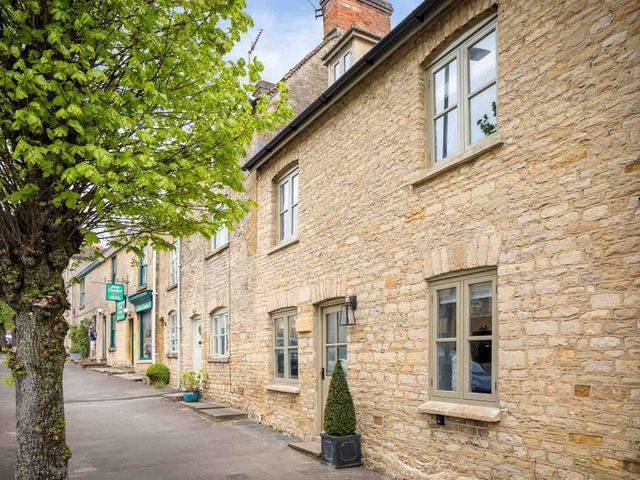 A stone house with windows and a door with a sign at Lavender Cottage in Cheltenham