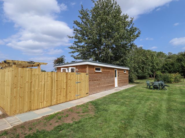 A shed with a fence and seating in a garden at Pear Tree Lodge in Alford