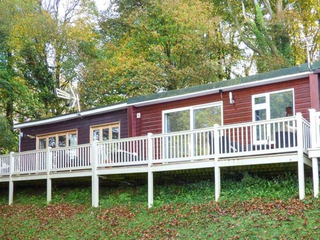 A wooden cabin with a deck surrounded by trees at I C Lundy Too Bideford Bay Holiday Park near Clovelly