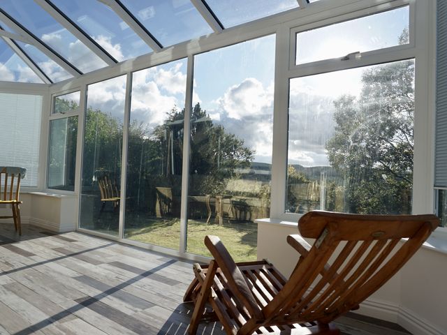A conservatory with wooden chairs and glass panels at The Peak View Holmfirth