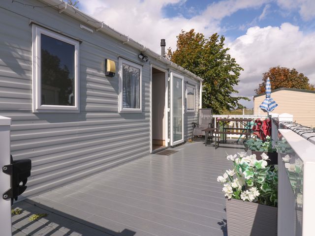 An outdoor porch with a door, chairs, and planters at Singh and Leite Family Caravan St. Osyth