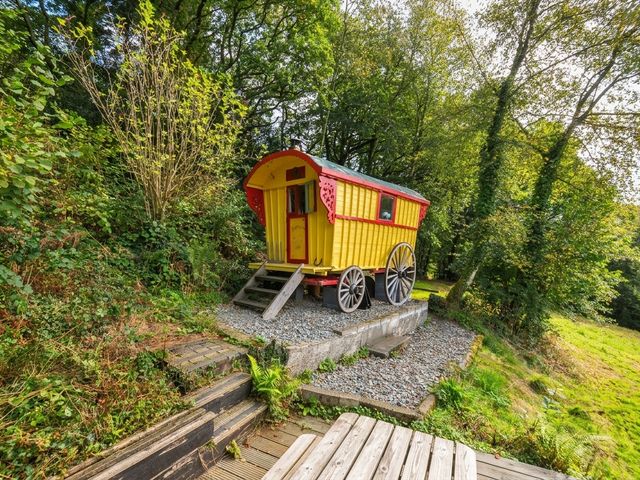 A gypsy caravan on a gravel base surrounded by trees and grass at Prudence Panson Mill near Ashwater