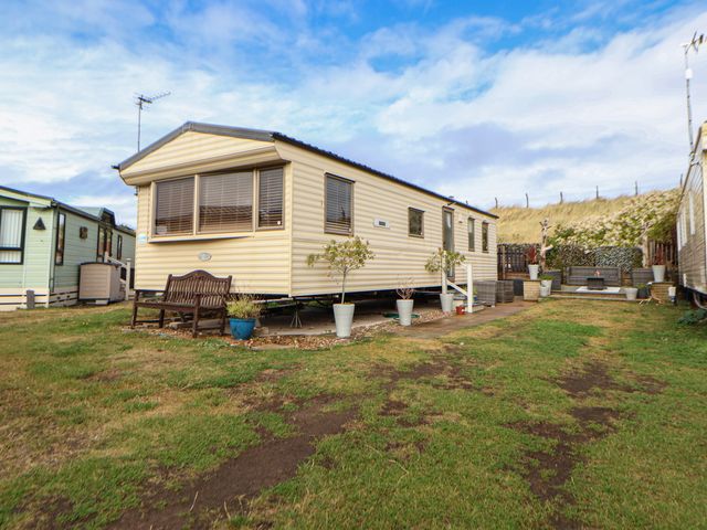 An outdoor view of a caravan with a bench and flower pots at Caravan 596 in Prestatyn
