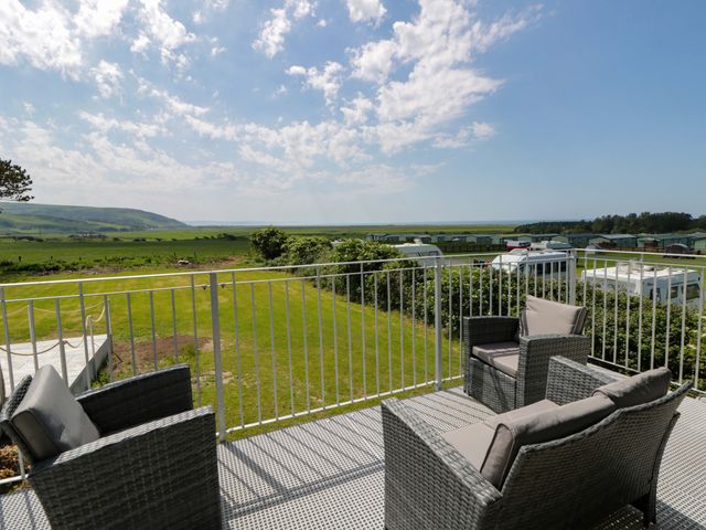 A balcony with chairs overlooking a grassy area and hills at Rosemary Cottage 2 Tywyn