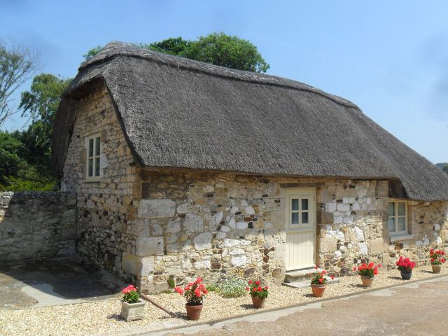 A stone cottage with a thatched roof and flower pots at Sheepwash Barn