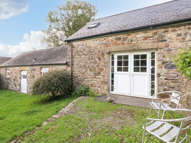 An outdoor area with a stone wall, double doors, and chairs at Rafters Cottage, Clarbeston Road