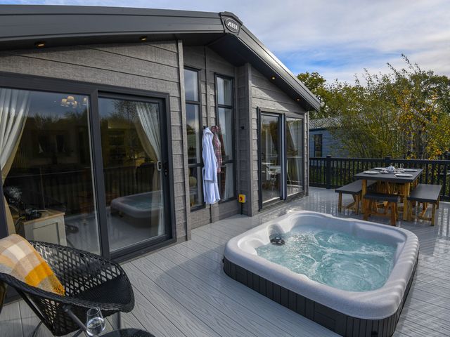 An outdoor terrace with a hot tub and dining table at Lakewood Retreat Woodhall Spa