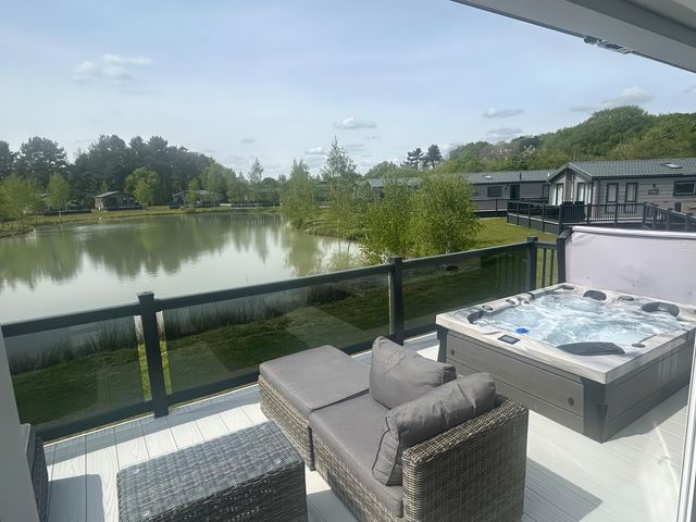 An outdoor area with a hot tub and sofa overlooking a lake at Hotchkin Lodge Woodhall Spa