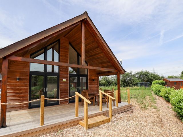 A wood cabin with a deck and seating area at Lodge 12 in South Hykeham
