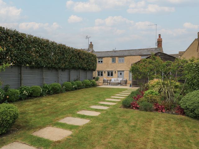 A garden with a house and pathway at The Cottage in Ashton Keynes