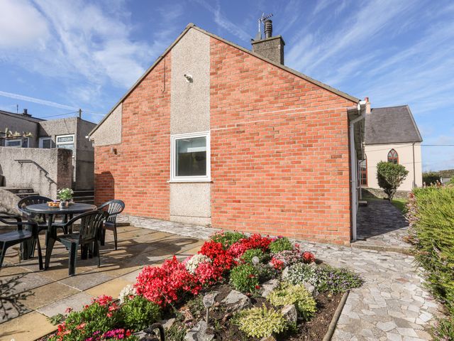 An outdoor area with a table and chairs next to a flower bed at Gelli - Morfa Nefyn