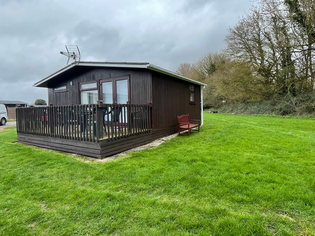 A brown cabin with a deck and bench at Hoburne Cotswolds - Holiday Accommodation 10757 Cirencester