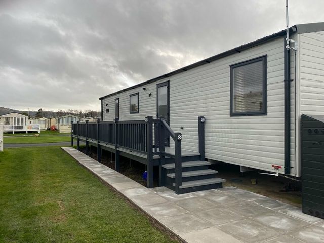 a caravan with a deck and steps on a grassy area at Lido Beach Holiday Park - Holiday Accommodation 12350, Prestatyn