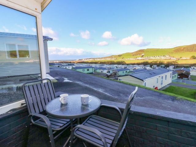 A balcony with a table and chairs overlooking a caravan park and hills at Captain's Cabin, Clarach Bay near Aberystwyth