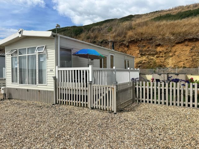 A mobile home with a deck and fence at Freshwater Beach Holiday Park - Holiday Accommodation 17116 in Burton Bradstock near Bridport
