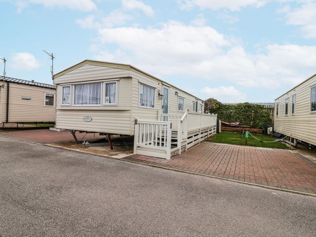 A static caravan with a decking area and paved driveway at Golden Gate Holiday Centre - Holiday Accommodation 20618 Abergele