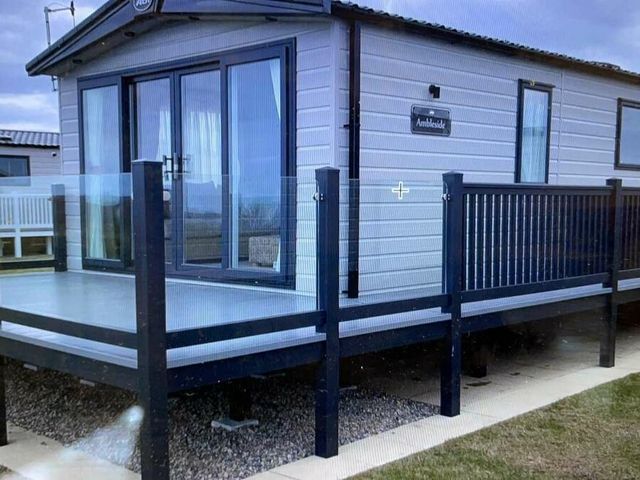 a cabin exterior with a deck and glass railings at Primrose Valley Holiday Park - Holiday Accommodation 21010 in Filey