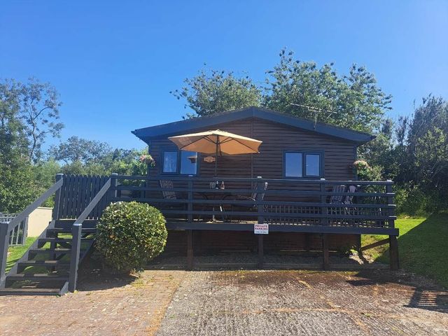 a wooden holiday cabin with a deck and umbrella at Quay West Holiday Park - Holiday Accommodation 21392 New Quay