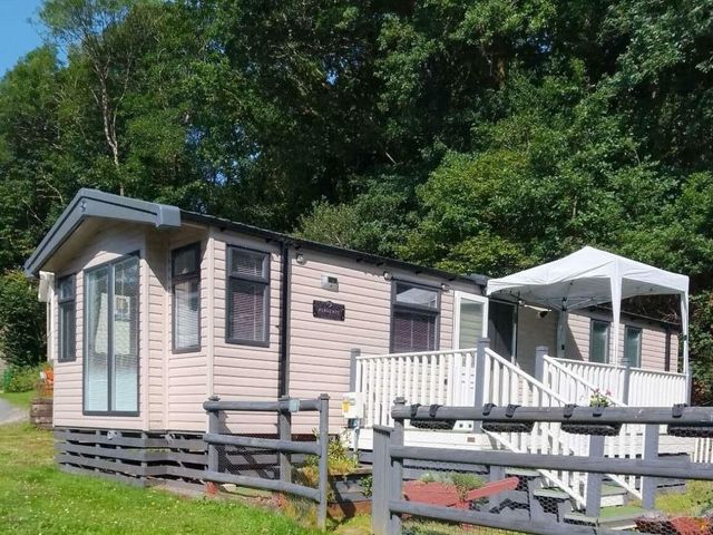 a holiday home with a small porch and a canopy surrounded by trees at Aberdunant Hall Holiday Park - Holiday Accommodation 22229 Porthmadog