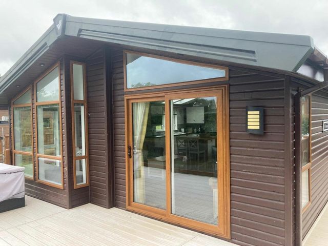 an exterior view of a modern lodge with large windows and a deck at White Acres Holiday Park - Holiday Accommodation 22327, Whitecross, Newquay