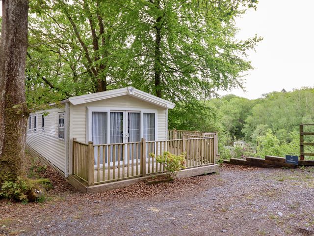 A mobile home with a deck surrounded by trees at 145 Woodside View in Porthmadog