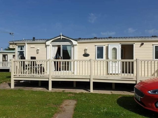 a mobile home with a deck and a red car in front at Coral Beach - Holiday Accommodation 22375 in Ingoldmells