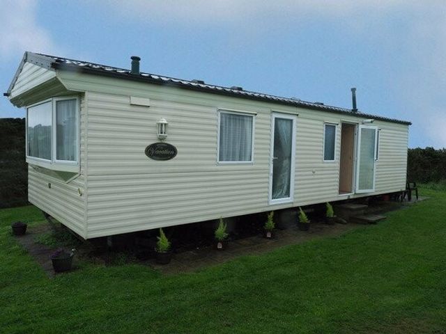 a caravan with a light-colored exterior and a small porch at Nine Wells Caravan Park - Holiday Accommodation 5912 Solva