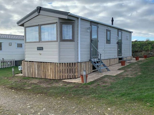 a static caravan with steps and a fence at Nine Wells Caravan Park - Holiday Accommodation 6373 in Solva