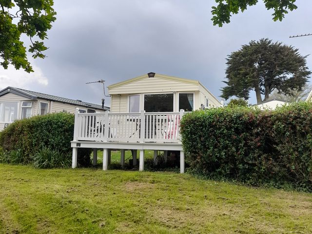 A static caravan with decking and a hedge at Devon Cliffs Holiday Park - Holiday Accommodation 7643 in Exmouth
