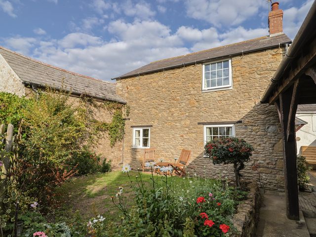 A garden with chairs and flowers at Vine Cottage in Burton Bradstock