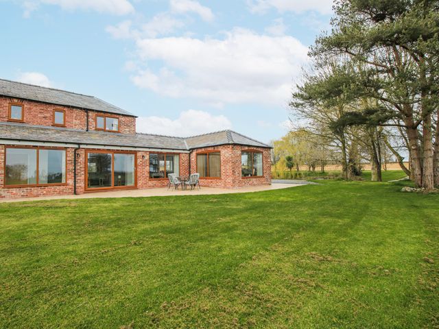 An outdoor view of a brick house with a patio and surrounding grass at Garden Cottage in Cockshutt